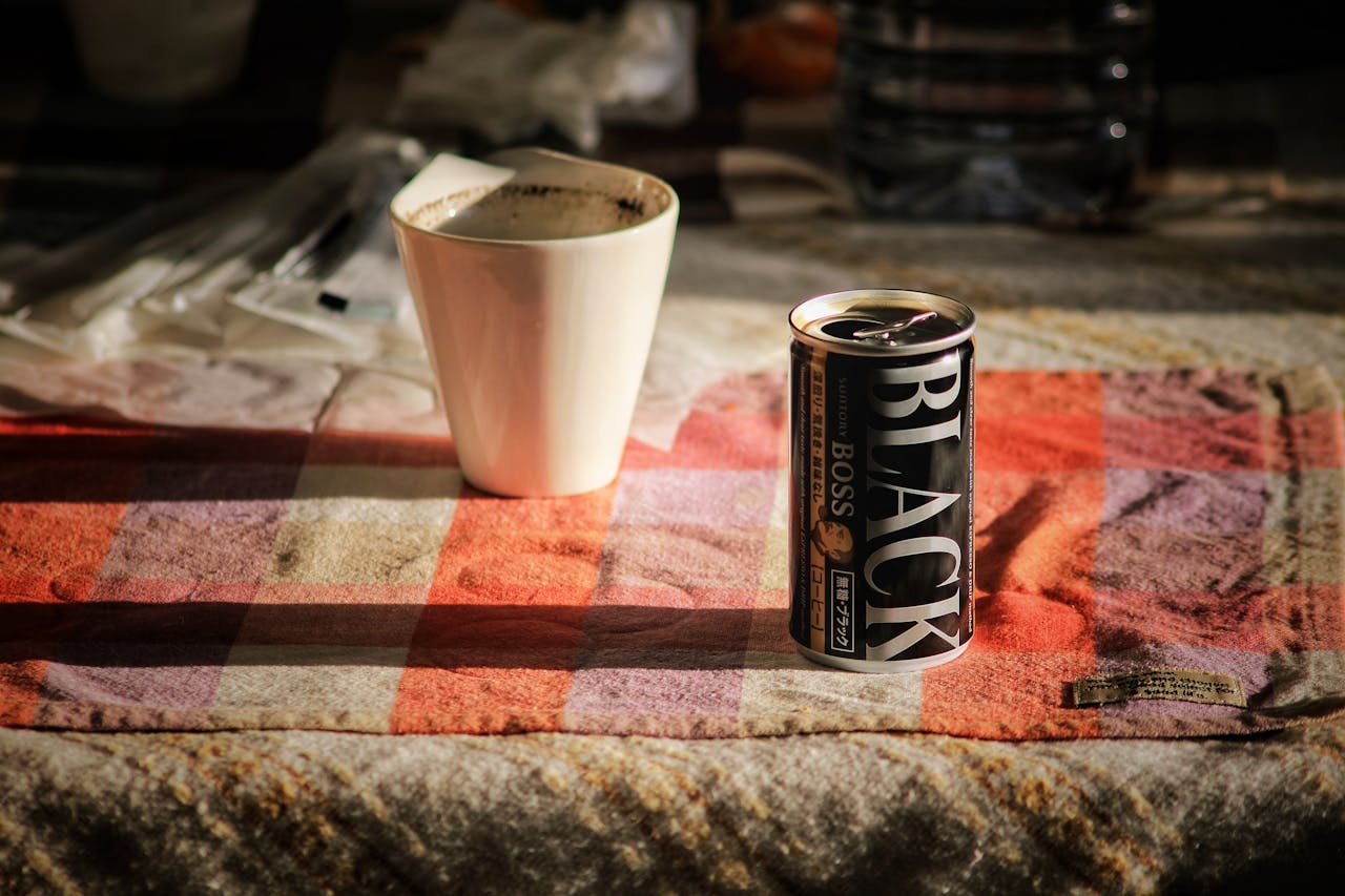 Close-up of a can of black coffee and a porcelain mug on a checkered tablecloth.