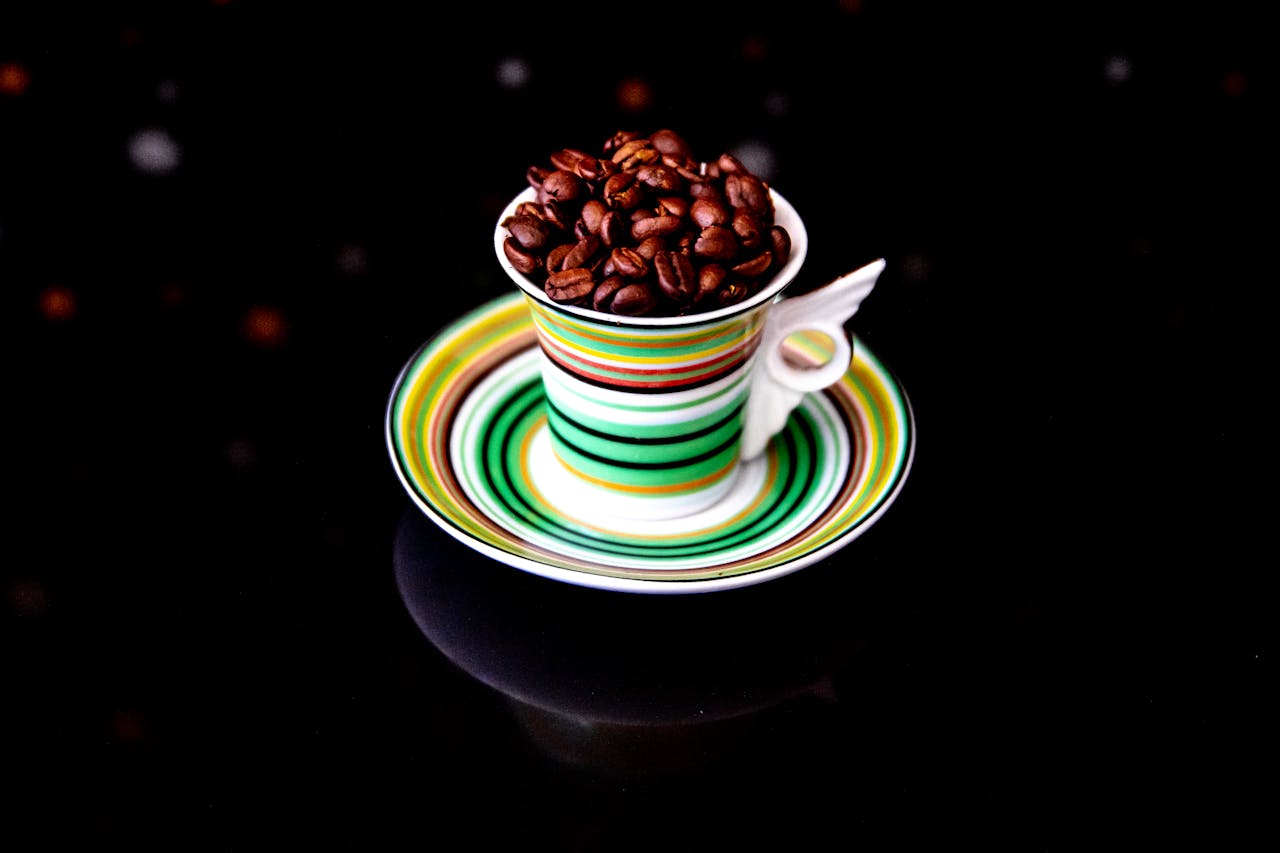 Close-up of coffee beans overflowing a colorful striped cup and saucer.